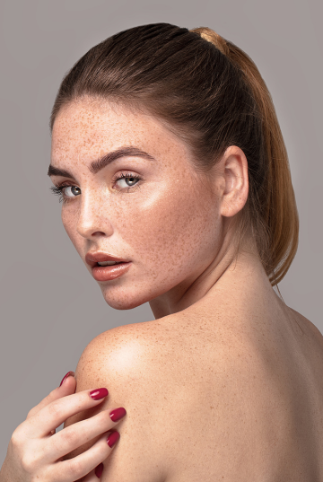 Over the should portrait of a lightly tanned model who has auburn hair in a ponytail and freckles.
