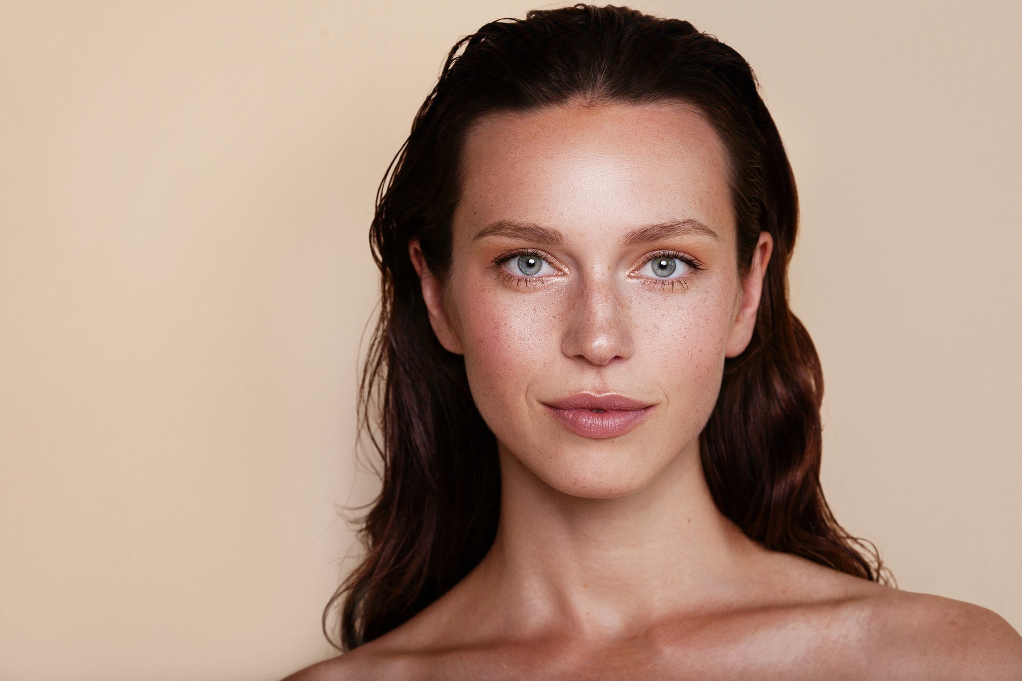 Neck up portrait of a white woman  with glowing skin, freckles, green eyes, and brushed back reddish brown hair