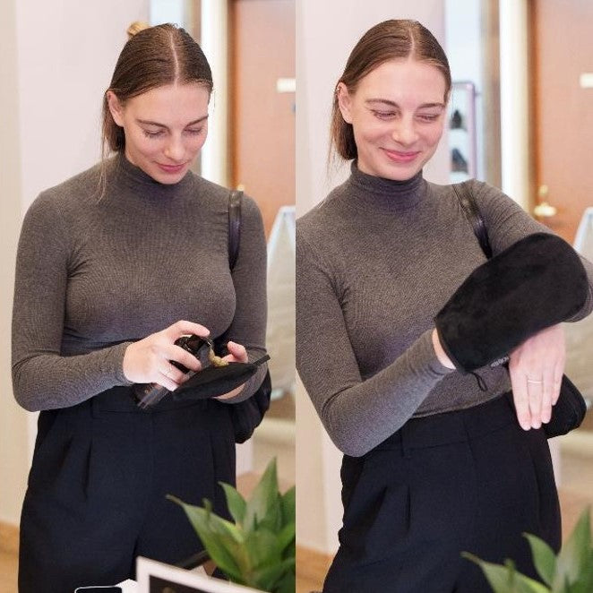 Woman wearing a gray turtleneck sweater and black pants applying self-tanner