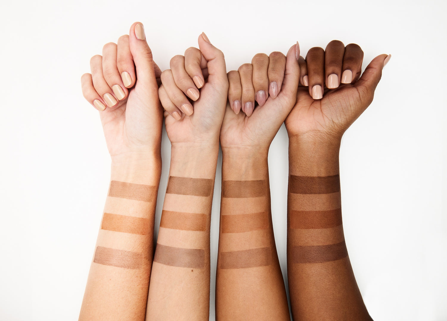 Four models arms arranged from light to dark skin tone arms with spray tan color swatches on their forearms. 